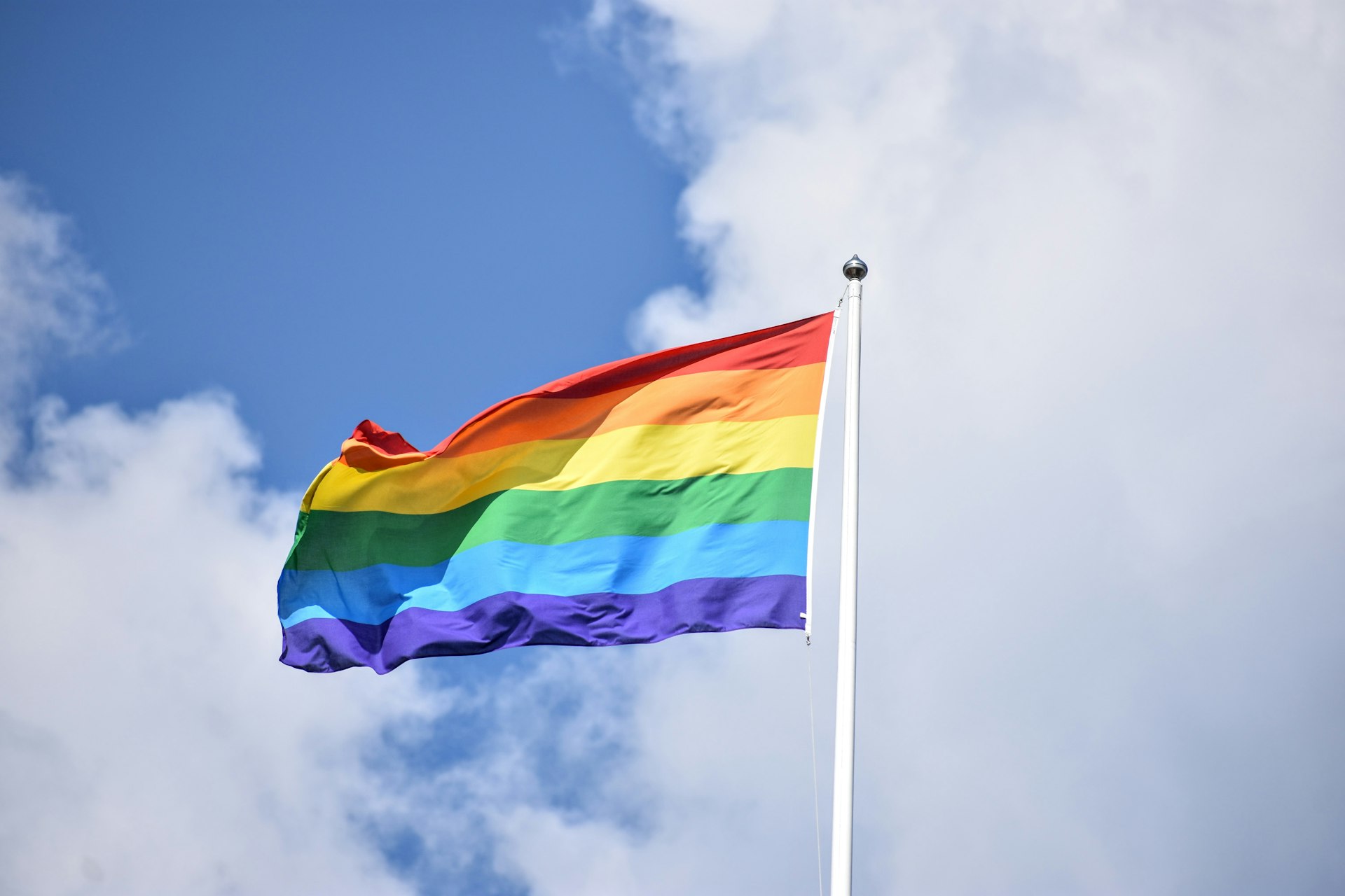 A rainbow Pride flag flying against a blue sky