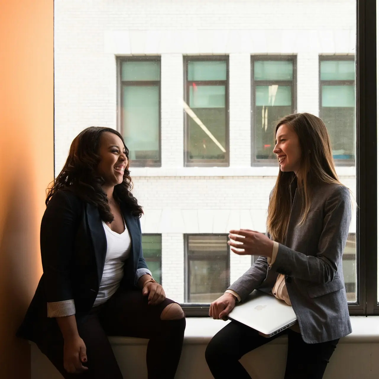 two woman sitting by the window laughing