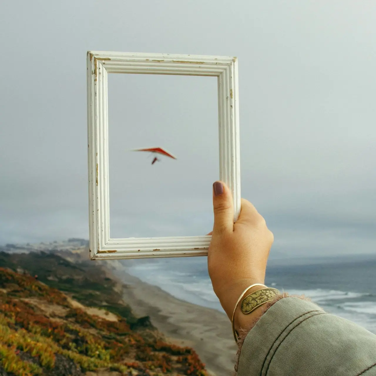 person holding rectangular white photo frame standing on rock formation near body of water